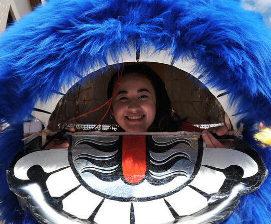 Lion dancer smiling through the mouth of a blue lion head.