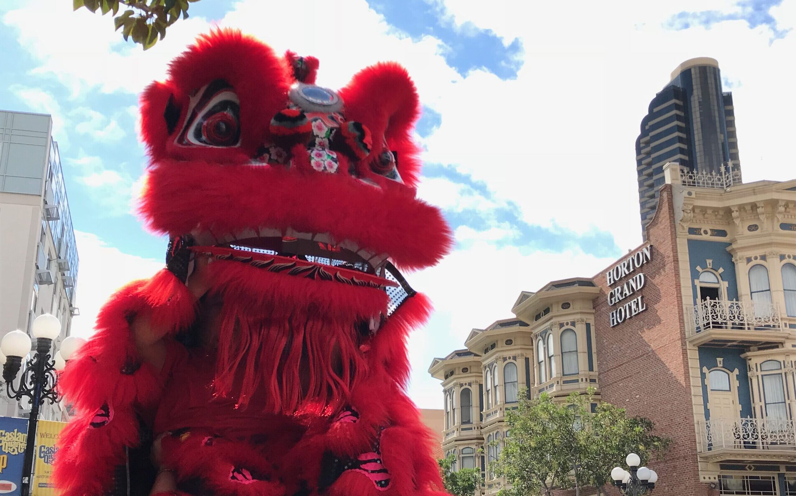 Lion dancers doing a "head set" where lion dancer holding the lion head is seated on the head of the person performing tail with the Horton Grand Hotel in the background